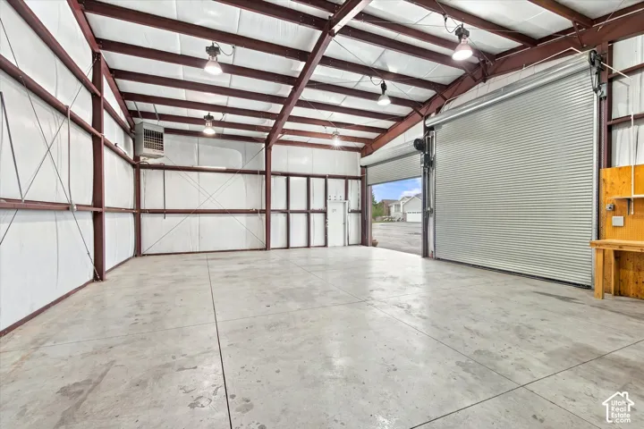 Expansive warehouse space featuring exposed steel beams, high ceilings, polished concrete flooring, a motorized roll-up door, and industrial-style overhead lighting