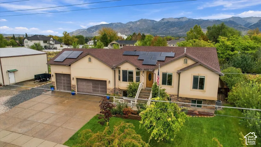 Single-story residence featuring a multi-gabled roofline with integrated solar panels, stone and stucco exterior, attached garage, and mountain backdrop