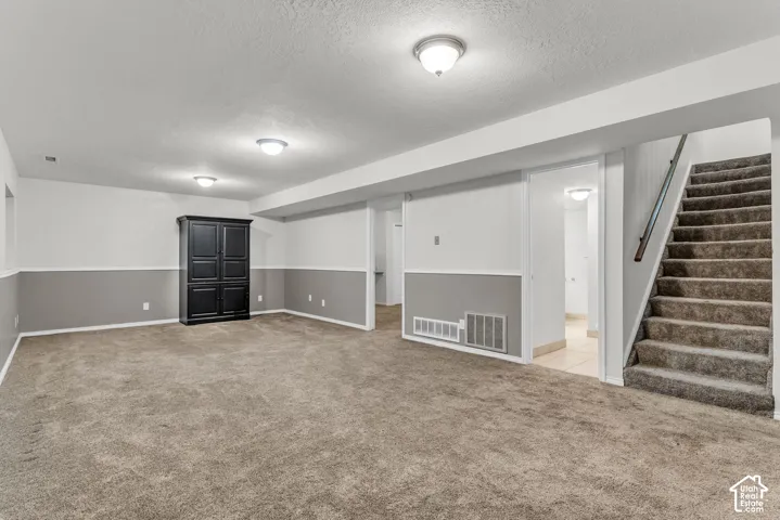 Neutral-toned interior space featuring carpeting, two-toned wall paint with chair rail molding, and staircase with metal handrail