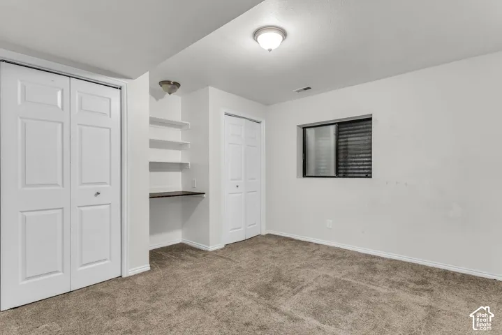 Room featuring neutral carpeting, dual closets with white bi-fold doors, and a built-in workspace with integrated shelving
