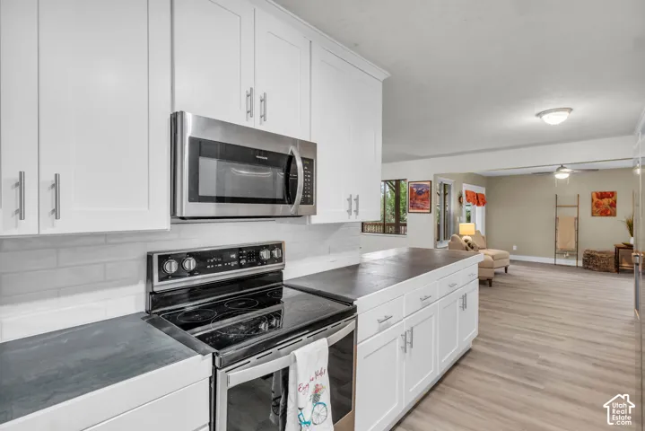 Kitchen featuring shaker-style cabinetry, matte countertops, stainless steel electric range, over-the-range microwave, and wood-finish flooring