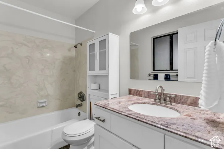 Bathroom featuring a stone-topped vanity with an oval undermount sink, brushed nickel faucet, large wall-mounted mirror, and tub-shower combination with patterned wall surround