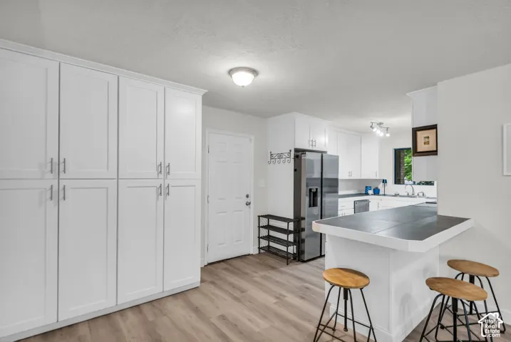 Kitchen featuring white shaker-style cabinetry, wood-finish flooring, a tile-topped peninsula, and stainless steel appliances