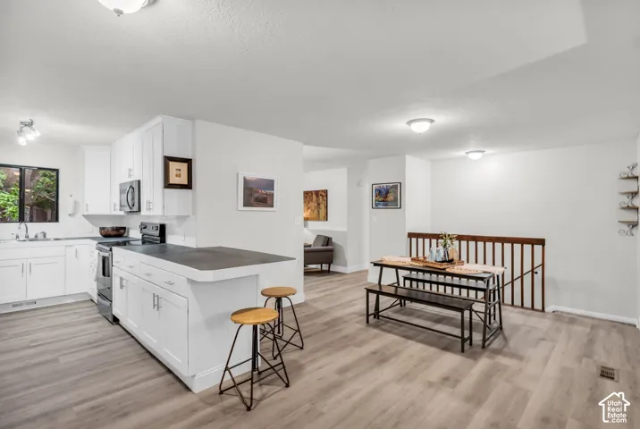 Kitchen featuring white shaker-style cabinetry, dark solid-surface countertops, wood-finish flooring, and a stained wood stair railing