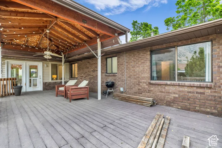 Expansive rear patio featuring brick exterior walls, a covered wooden pergola, wood-finish decking, and a ceiling fan