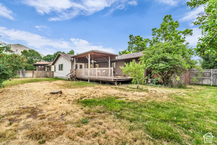 Rear exterior featuring a covered wood deck, brick and siding facade, and fenced grounds