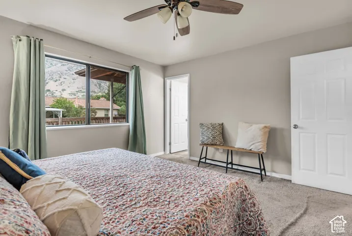 Neutral interior space featuring carpeted flooring, a ceiling fan with integrated lighting, a six-panel door, and a large window showcasing a mountain backdrop