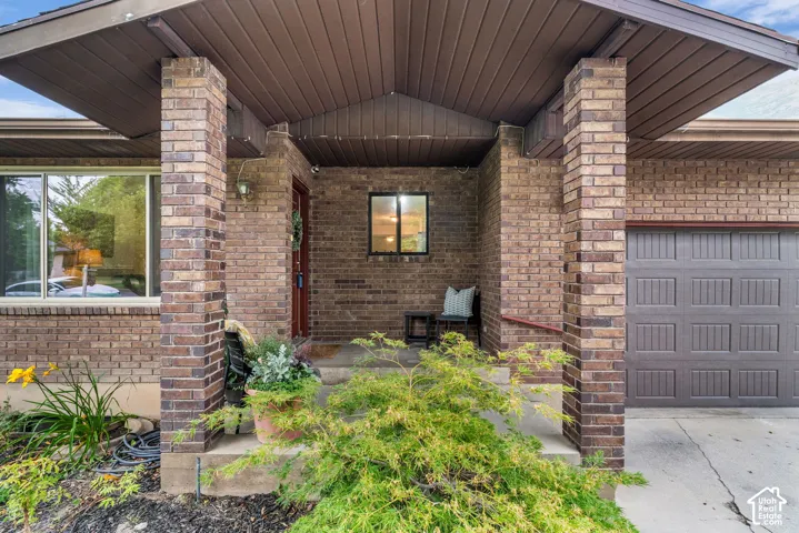 Covered entryway featuring brown brick masonry, supporting pillars, a peaked roofline, and a panelled garage door
