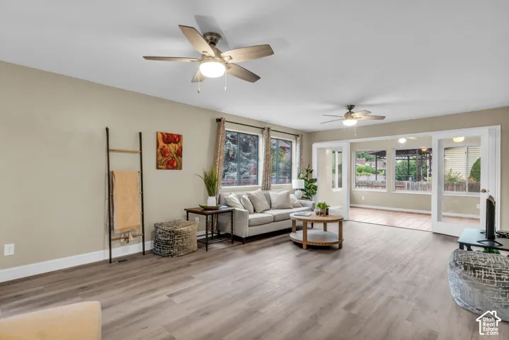 Spacious room featuring wood-finish flooring, two ceiling fans with integrated lighting, and glass-paneled exterior doors