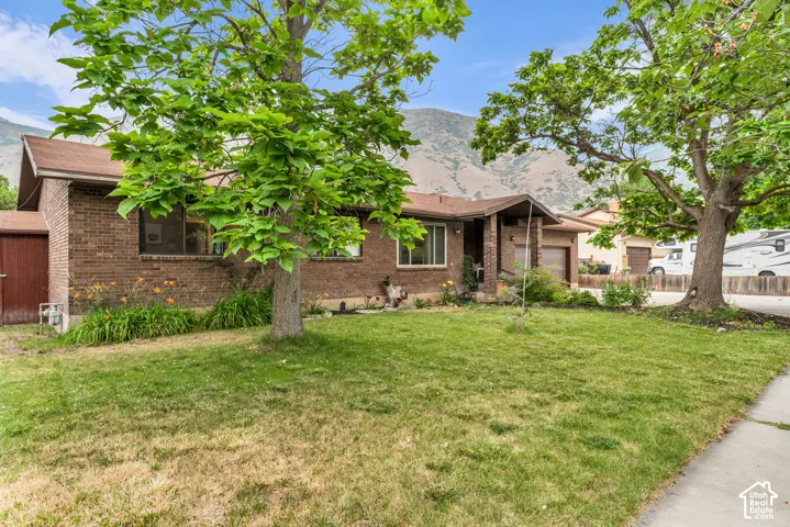 Single-story brick exterior featuring a low-slope roof, attached garage, and mature trees against a mountain backdrop