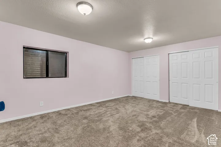 Interior space featuring neutral-tone carpeting, dual sliding-panel closet doors, and a rectangular window with dark-toned framing