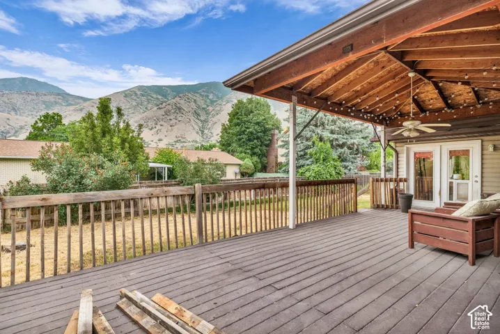 Spacious elevated deck featuring a wood-plank surface, wood railing, and an expansive covered patio area with exposed rafters and a built-in ceiling fan, set against a mountain backdrop