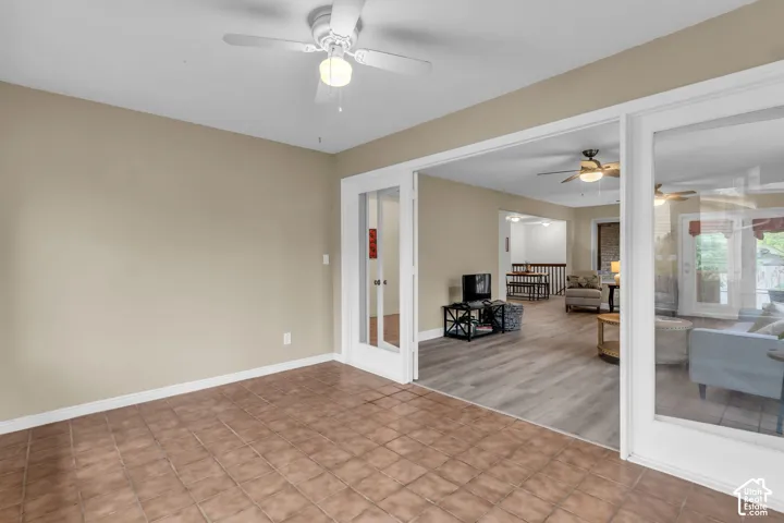 Room featuring tile flooring, ceiling fan with integrated light fixture, wood-finish flooring, and white glass-paneled French doors