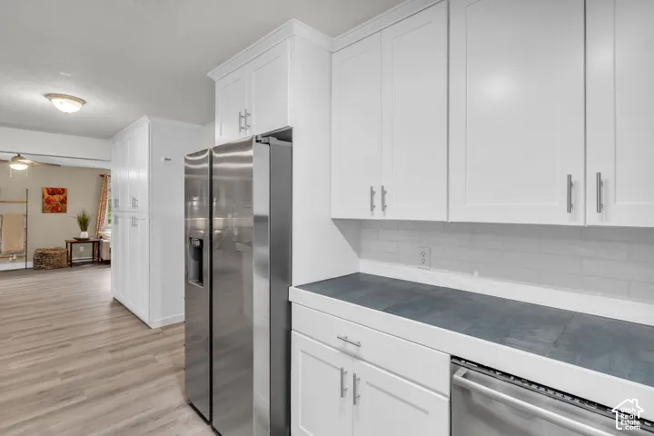 Kitchen featuring white shaker-style cabinetry, stainless steel appliances, dark stone-surface countertops, and light-toned wood-finish flooring