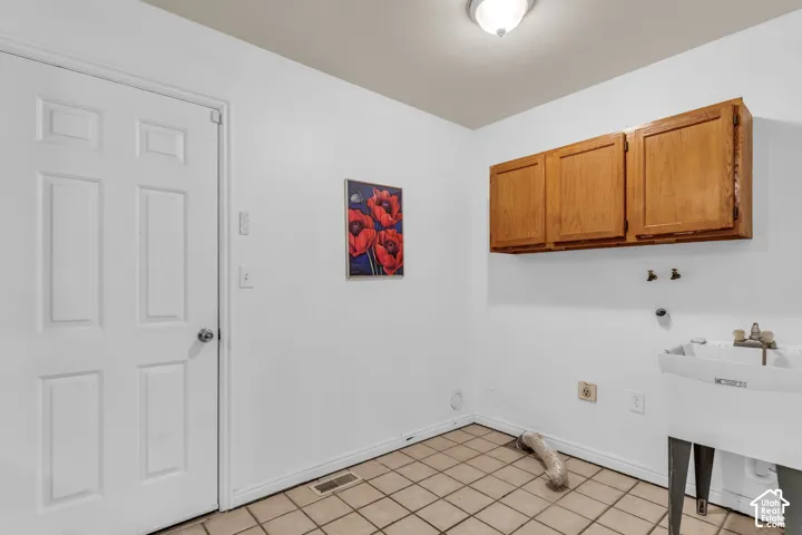 Utility room featuring ceramic tile flooring, built-in wooden wall-mounted cabinetry, a free-standing utility sink, and a six-panel door