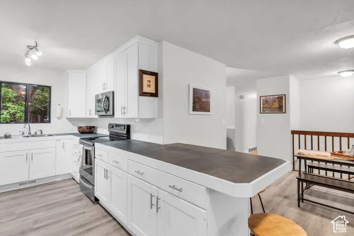 Kitchen featuring white shaker-style cabinetry, a breakfast bar with dark countertops, wood-finish flooring, and stainless steel appliances