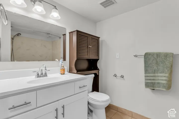 White vanity with a solid-surface integrated sink, chrome dual-handle faucet, full-width mirror with a three-light fixture, and ceramic tile flooring
