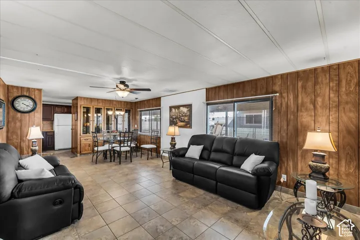 Open concept living area featuring wood-paneled walls, tile flooring, a ceiling fan, and built-in wood cabinetry