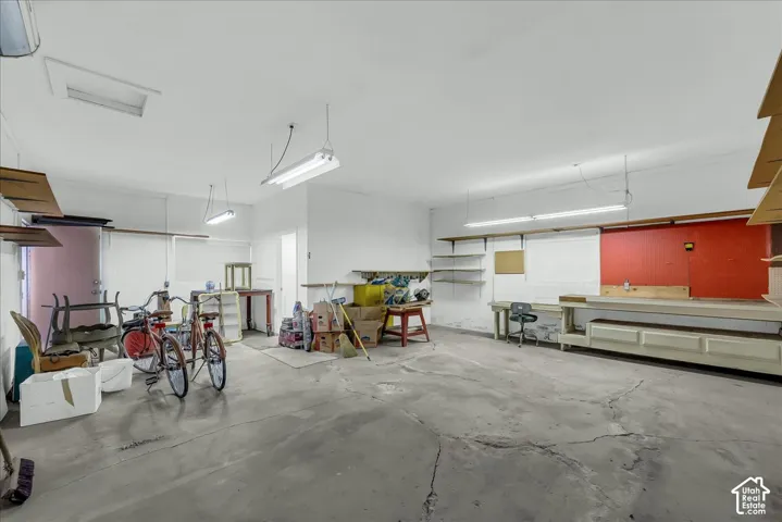 Multi-vehicle garage featuring a concrete floor, built-in workbench, overhead fluorescent lighting, and extensive wall-mounted shelving