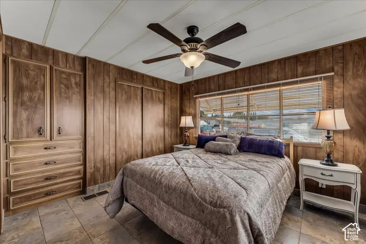 Wood-panelled walls, built-in cabinetry featuring integrated drawer storage, tile flooring, multi-pane window, and a central ceiling fan with an integrated light fixture
