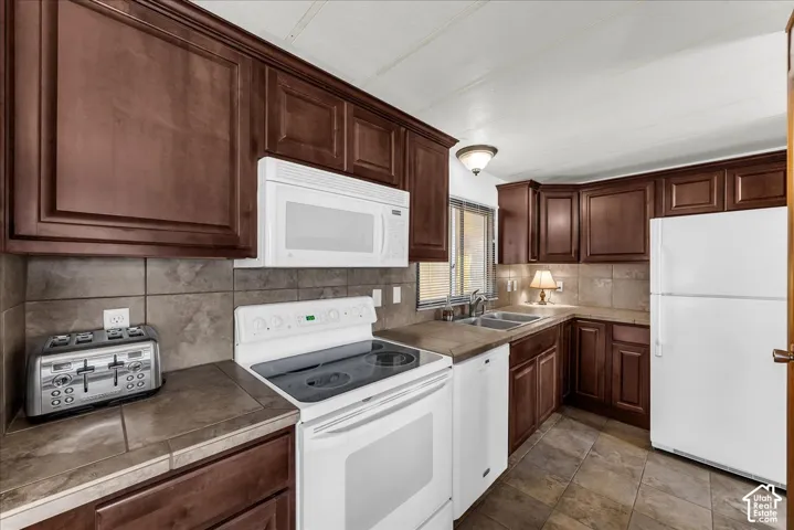 Kitchen featuring stained wood cabinetry, tile backsplash, tile flooring, and white appliances