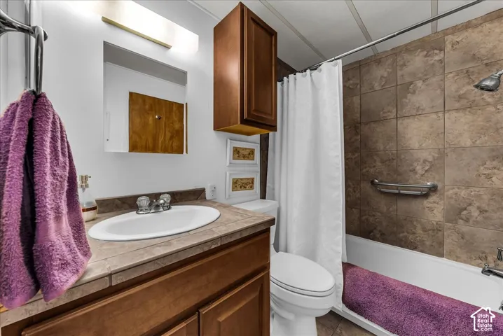 Bathroom featuring a wood-finish vanity with a tile countertop, an integrated oval sink, a wall-mounted wooden storage cabinet, and a shower-tub combination with tiled surround