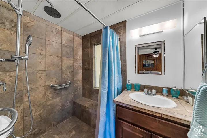 Walk-in shower featuring floor-to-ceiling tile, a built-in tiled bench, and a dual-head shower system including a rainfall fixture and handheld sprayer, complemented by a vanity with an integrated basin and tiled countertop