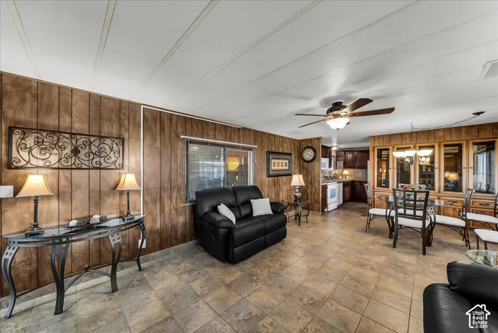 Open-concept interior featuring wood-panel wall treatments, large-format tile flooring, a ceiling fan with integrated lighting, and extensive built-in wooden cabinetry
