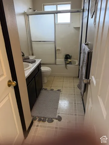 Bathroom featuring a vanity with dark cabinetry and a light-toned countertop, a shower-tub combination with sliding glass doors, and tiled flooring