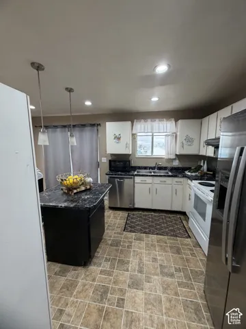 Kitchen featuring a central island with dark stone-finish countertops, white cabinetry, stainless steel appliances, recessed ceiling lighting, and patterned tile flooring
