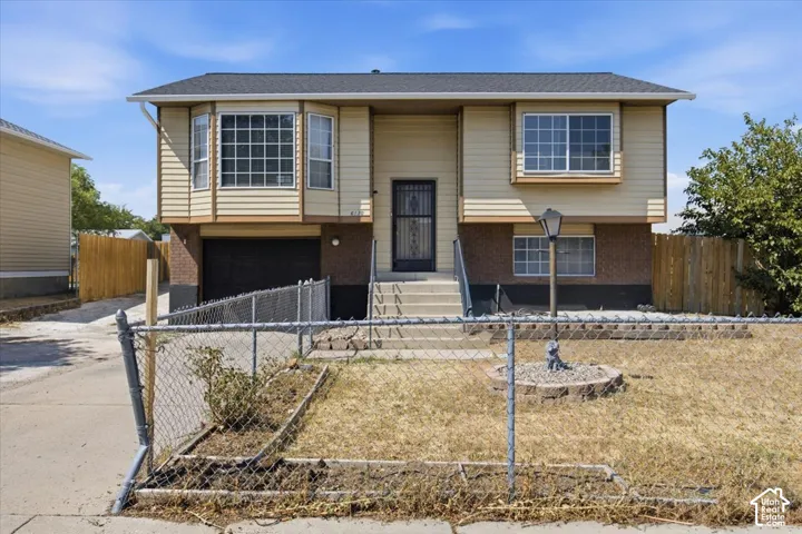 Bi-level exterior featuring horizontal siding, brick masonry, bay windows, an attached garage, and a gated perimeter