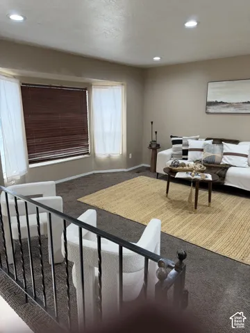 Bay window with neutral carpeting, recessed ceiling lighting, and wrought iron staircase railing