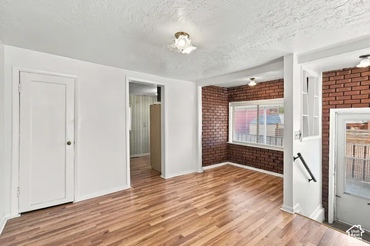 Wood-finish flooring throughout, white painted walls, exposed brick accent walls, and a window with blinds