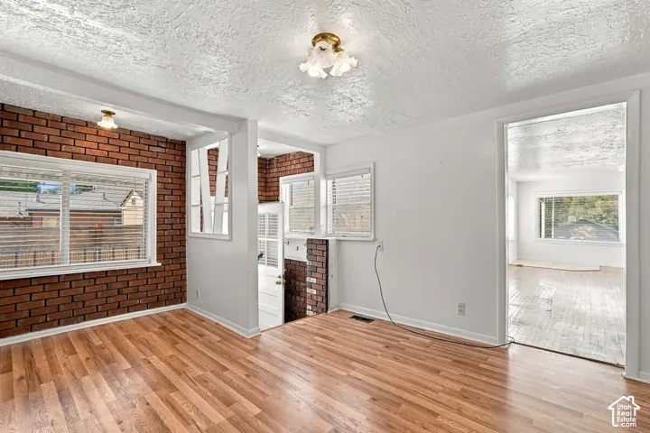 Hardwood-finish flooring, exposed brick wall, multiple windows with blinds, decorative ceiling light fixture, and white wall finishes