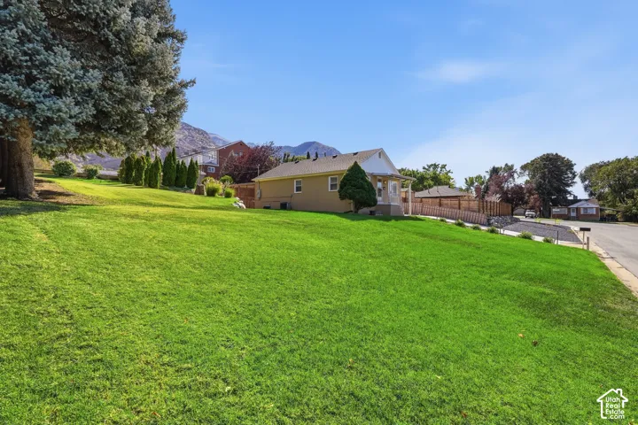 Expansive front yard featuring a manicured lawn, mature trees, and mountain scenery