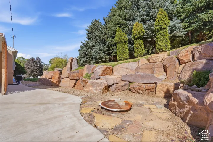 Tiered rock landscaping with mature evergreen trees and a paved concrete pathway