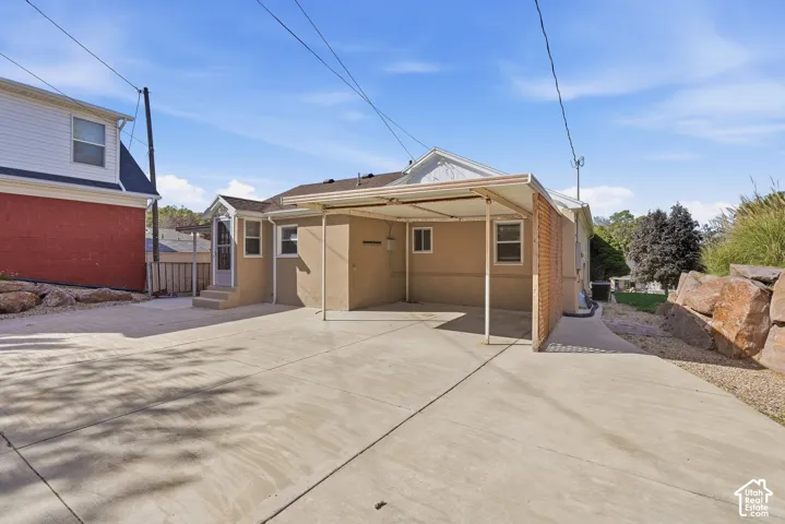 Expansive concrete driveway, attached carport, stucco exterior, brick accent wall, and stone retaining wall