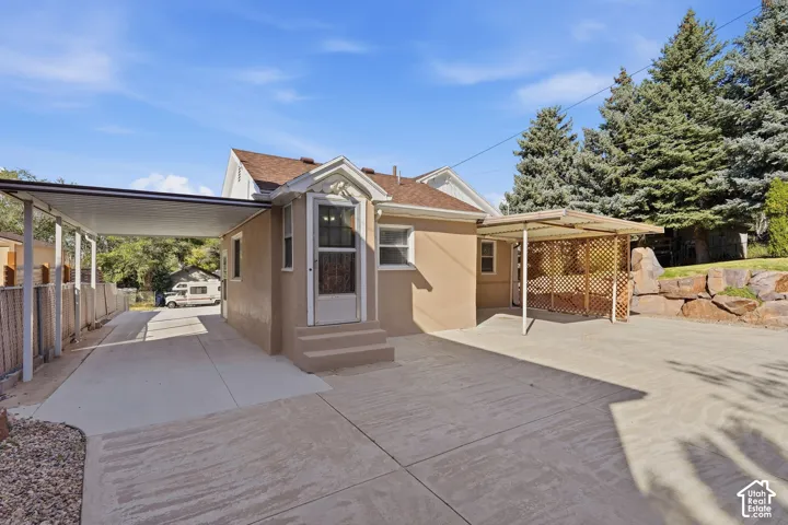 Stucco exterior, covered carport, concrete driveway, front entry with storm door, and a covered patio area