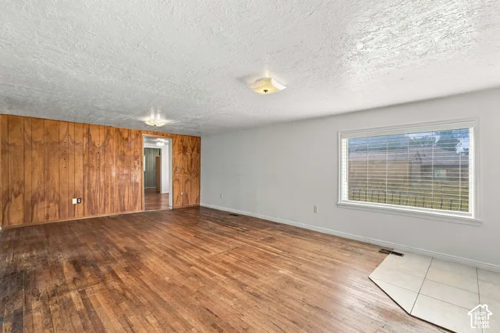 Wood-finish flooring, wood paneling, white painted walls, ceiling-mounted light fixtures, and a large window with blinds
