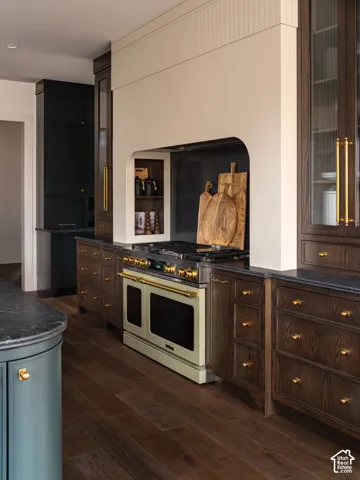 Built-in cabinetry with brass hardware, wood-finish flooring, integrated range with oven, custom range hood, and dark countertops