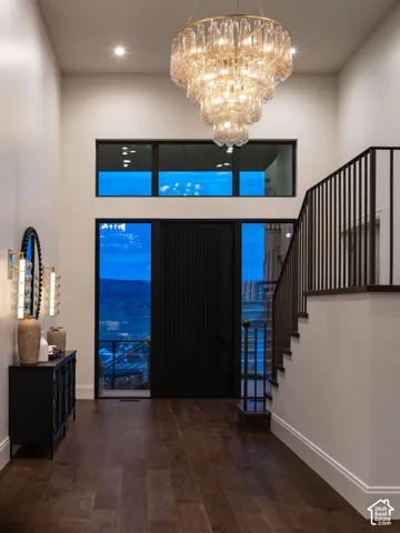Two-story foyer featuring a contemporary tiered chandelier, dark wood-finish flooring, a dark paneled entry door, and a staircase with dark iron railings
