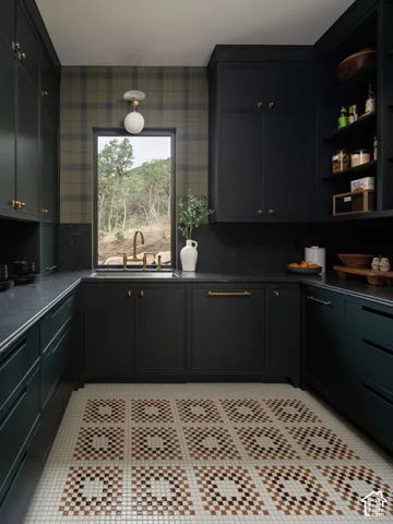 Custom dark cabinetry, dark countertops, patterned tile flooring, built-in shelving, and a wall-mounted light fixture