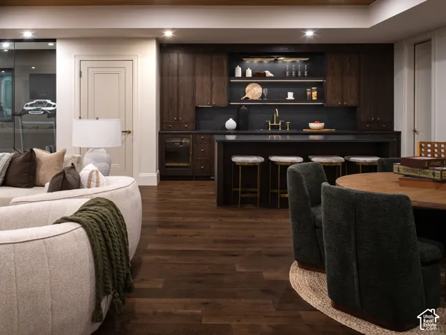 Wood-finish flooring throughout, dark wood-finish cabinetry, built-in shelving, integrated beverage refrigerator, and dark countertop with undermount sink