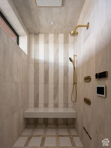 Spacious walk-in shower featuring a built-in bench, gold-finish fixtures, dual shower heads, and an integrated control panel