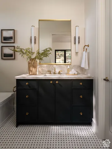 Black vanity with a light-toned countertop, gold-framed mirror, and a basketweave tile floor