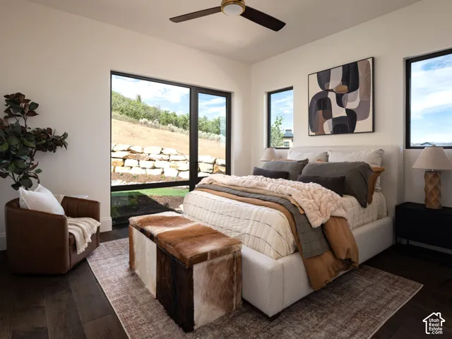 Expansive window offering abundant light, dark wood-finish flooring, overhead ceiling fan, white walls, and a stone retaining wall outside