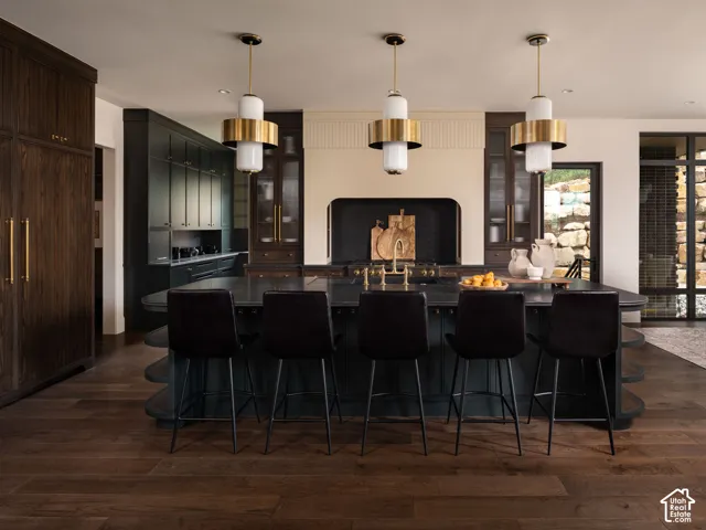 Expansive kitchen featuring a large island with seating, dark wood-finish flooring, custom dark cabinetry, and multiple pendant light fixtures