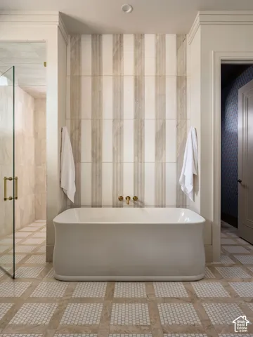 Freestanding soaking tub with wall-mounted brass fixtures, striped tile feature wall, and mosaic tile flooring