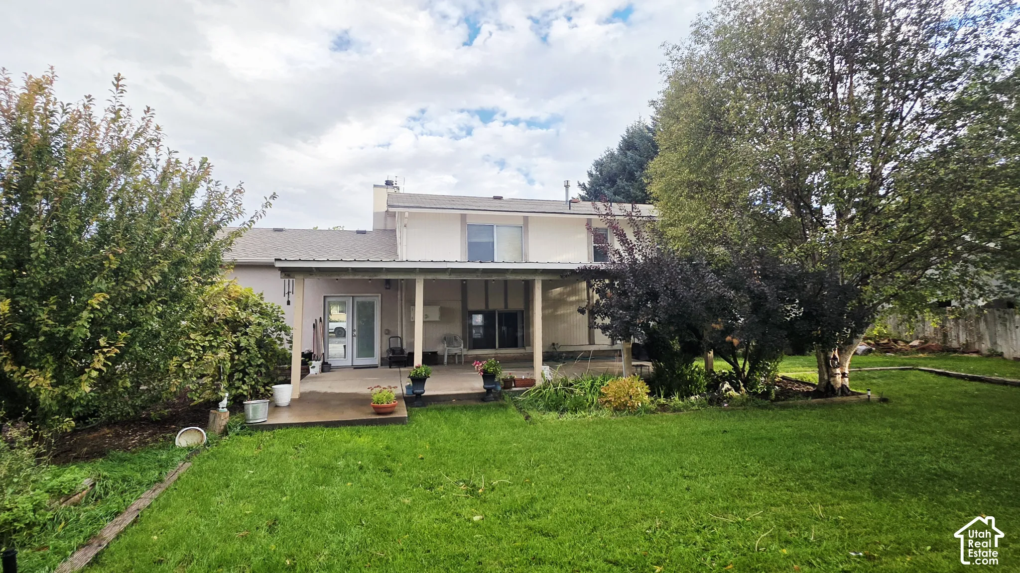 Rear exterior featuring a covered concrete patio, expansive lawn, and mature trees