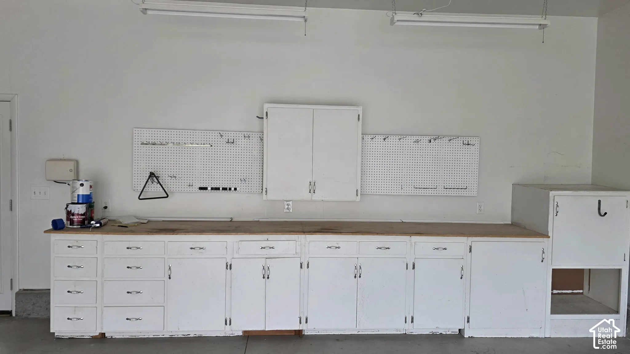 Built-in workbench with expansive wood-finish countertop, extensive lower cabinetry and drawers, wall-mounted storage cabinet, and dual integrated pegboard panels